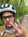Selfie of a man throwing up a peace sign in front of his face. He is wearing a bicycle helmet and appears to be on a bike trail.