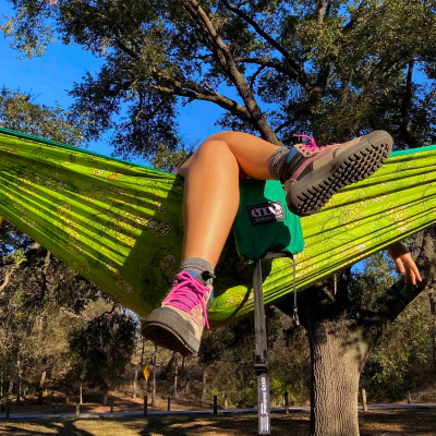 A person sits in a hammock with only their crossed legs visible, wearing colorful hiking boots. 